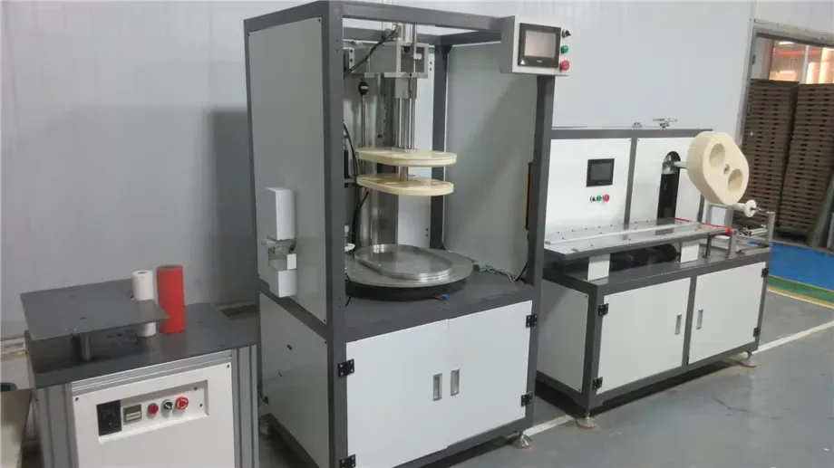 Turntable taping station sealing and finishing round parts before they join the scratcher line.