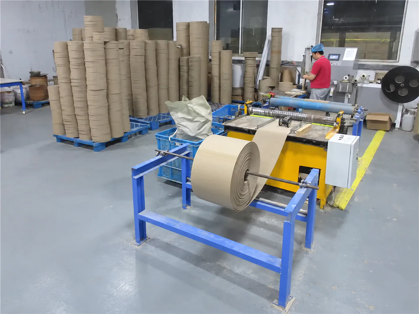 A kraft roll feeding the corrugated line, the raw face behind sturdy scratchers and lounges.